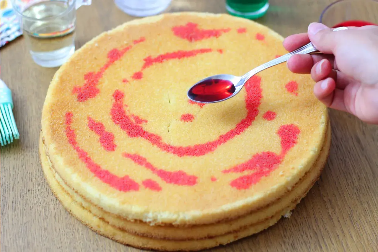 Un cucchiaino di sciroppo rosso viene versato su un pan di spagna a strati, decorato con un motivo a spirale.
