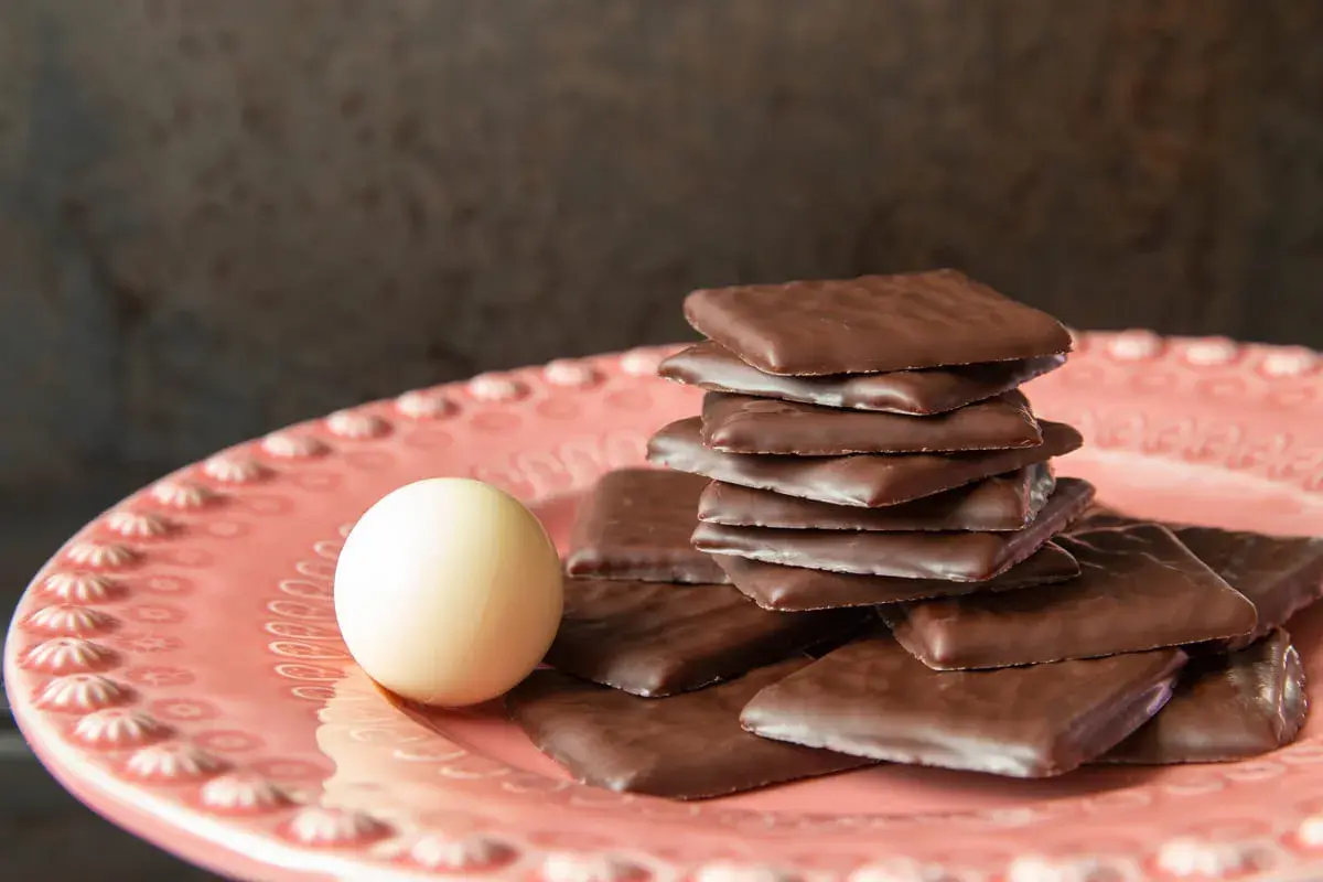 Piatto rosa con cioccolatini quadrati al cioccolato fondente e una pallina bianca. Un invito al gusto after eight.