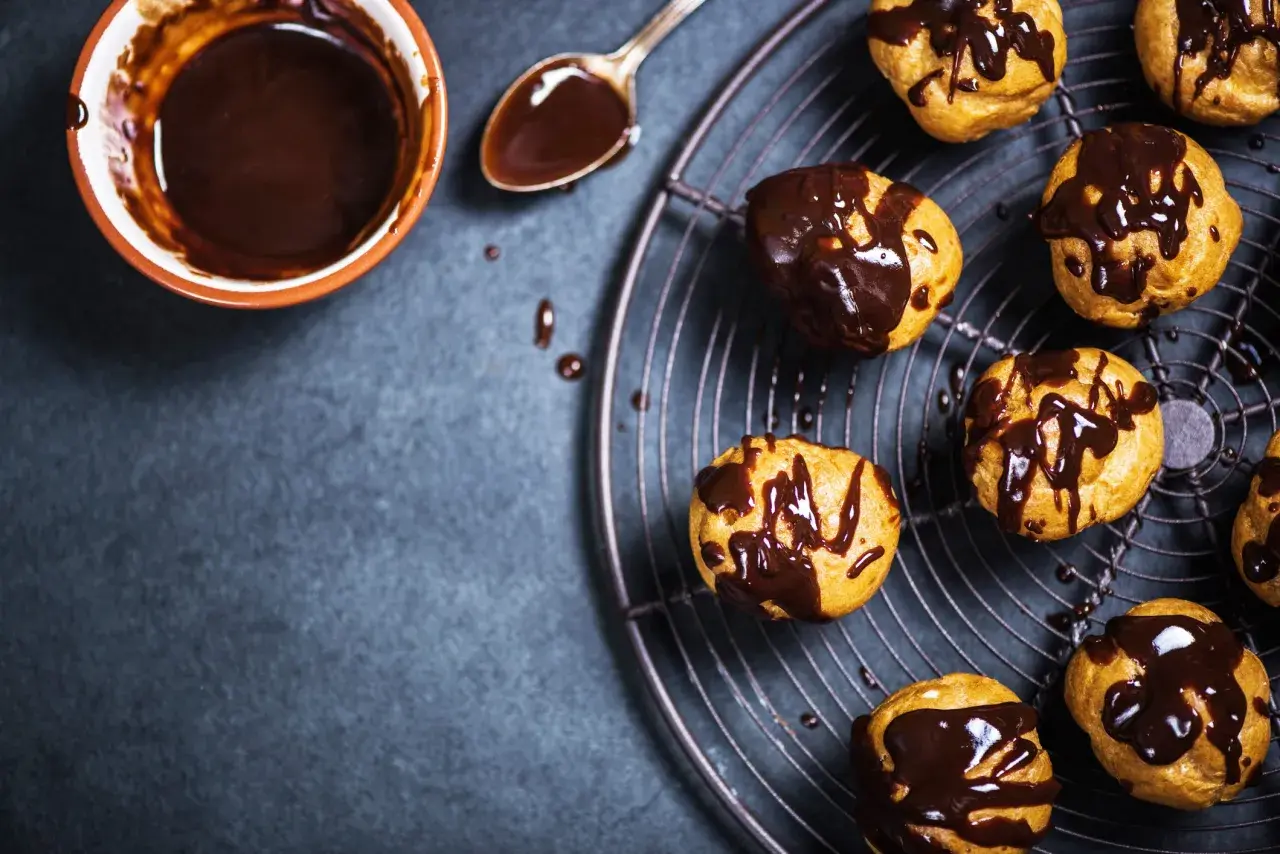 Profitterol ricetta: bignè dorati glassati con cioccolato fuso, pronti per essere gustati.