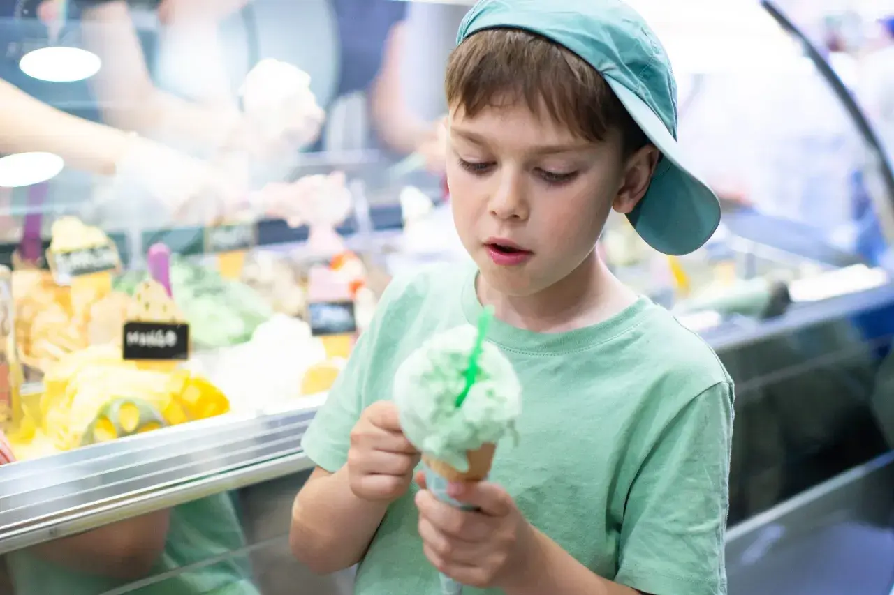 Bambino con cappellino azzurro gusta un gelato verde, pensando a chi ha inventato questa delizia.