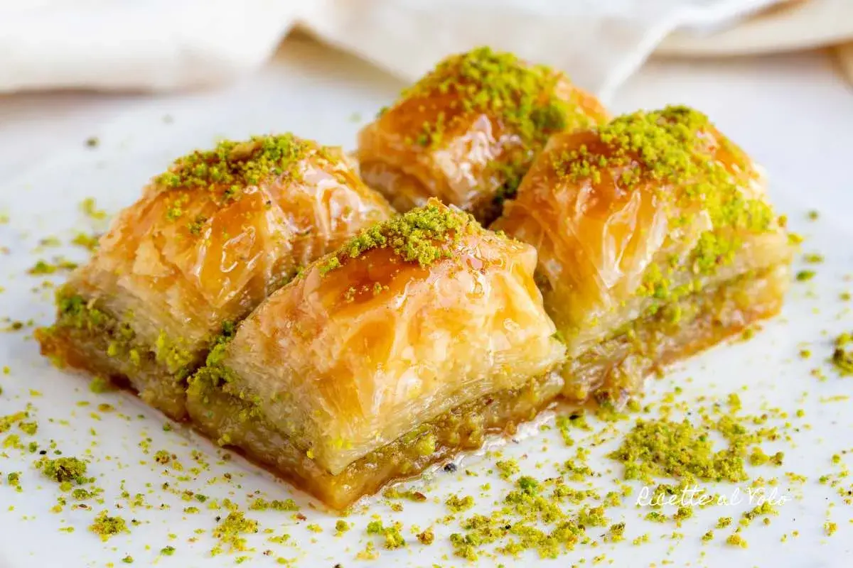 Quattro dolcetti di baklava, ricoperti di sciroppo dorato e pistacchi tritati, pronti per essere gustati.