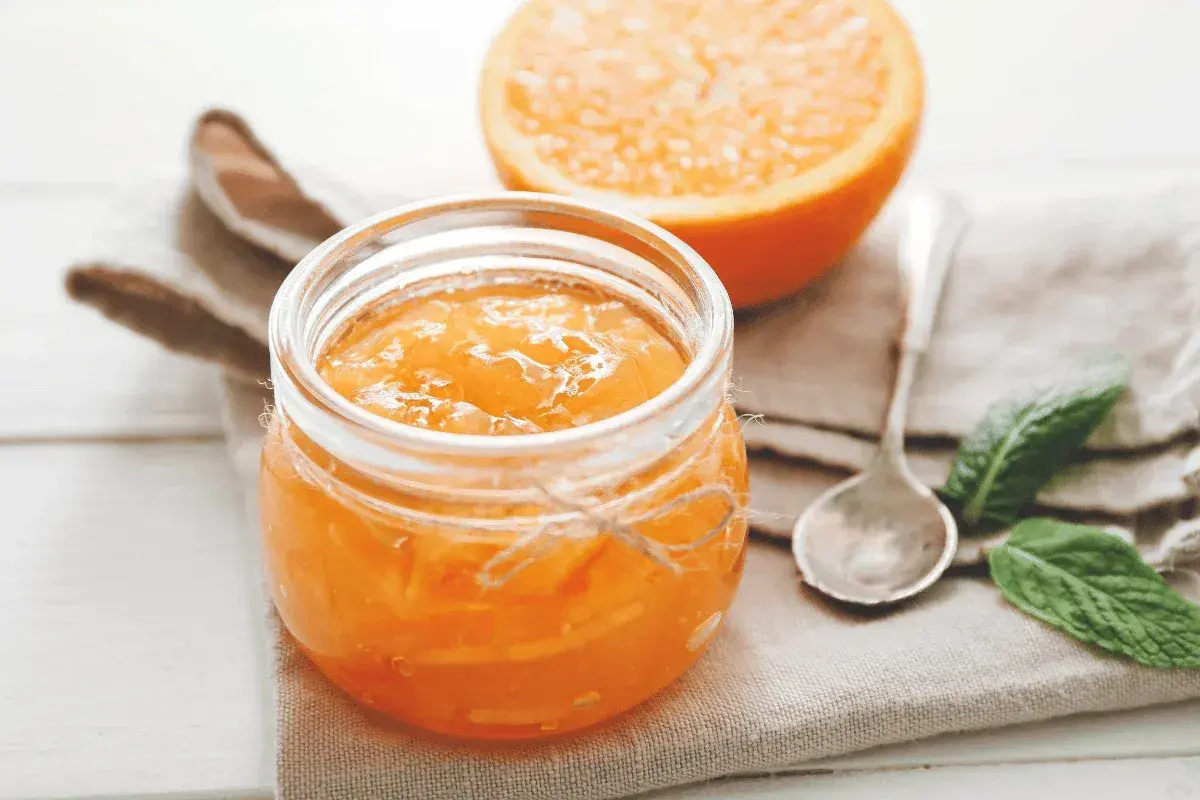 Barattolo di marmellata di arance fatto in casa, con una fetta d'arancia sullo sfondo.