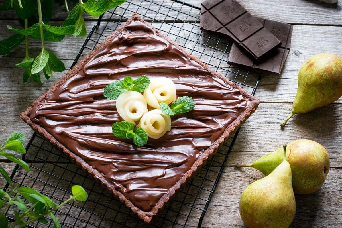 Torta quadrata al cioccolato con pere a rosa e menta. Un dolce goloso che unisce la cremosità della ricotta, la dolcezza delle pere e l'intensità del cioccolato.