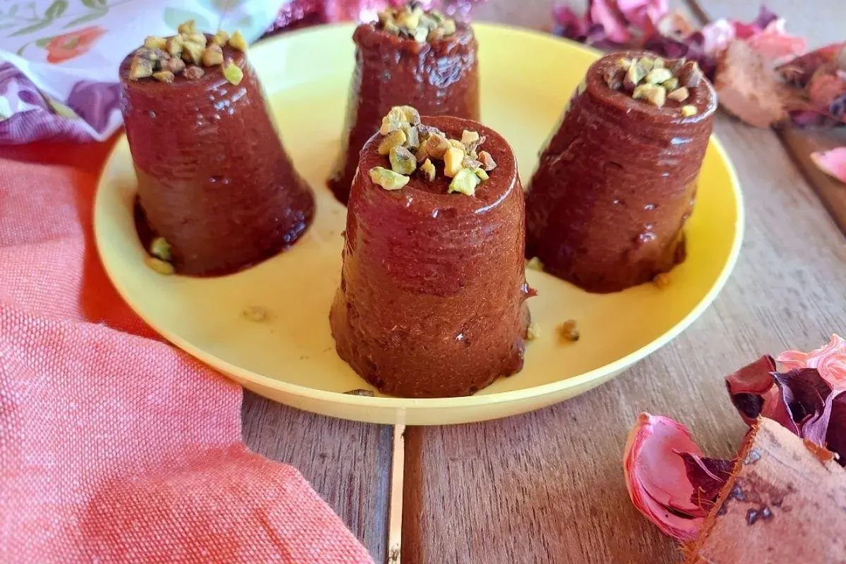 Quattro budini cachi e cacao, guarniti con pistacchi tritati, su un piatto giallo.