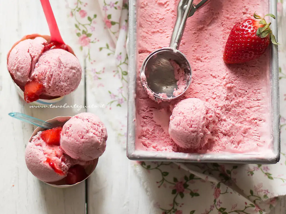 Coppette e vaschetta piene di cremoso gelato alla fragola, con fragole fresche e un cucchiaio pronto per servire.