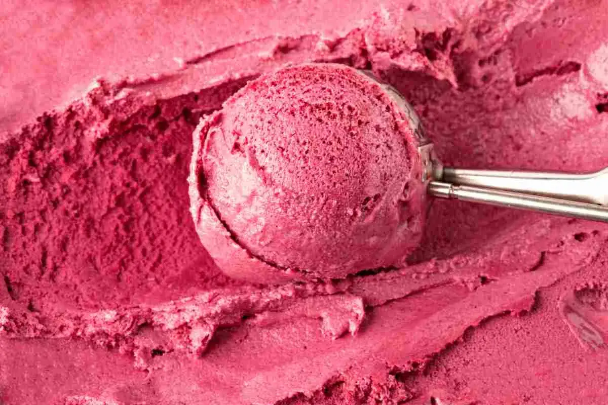 Un cucchiaio raccoglie un gelato rosa intenso, cremoso e invitante, preparato con latte e frutti di bosco.