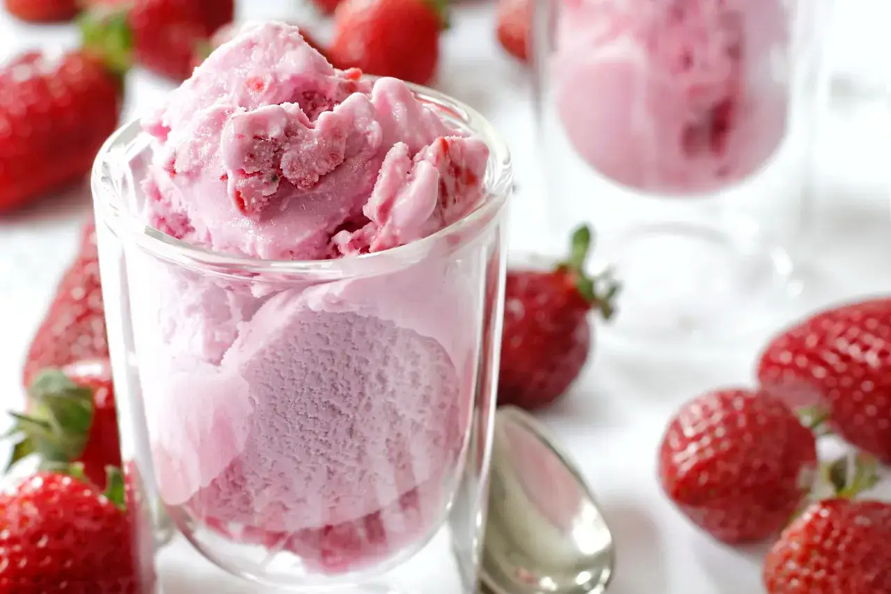 Un bicchiere pieno di cremoso gelato alla fragola, circondato da fragole fresche e succose.