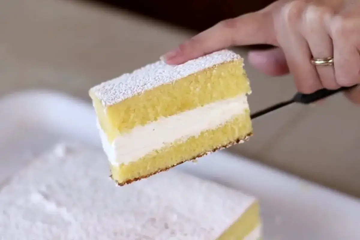 Una fetta di torta Kinder Paradiso, soffice e cremosa, viene sollevata da una spatola.