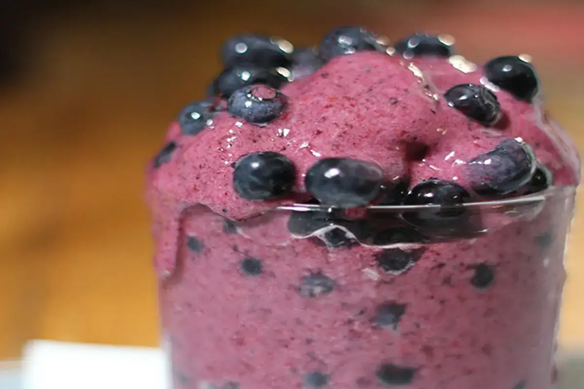 Sorbetto ai mirtilli, una delizia rosa con mirtilli freschi che cola da un bicchiere.
