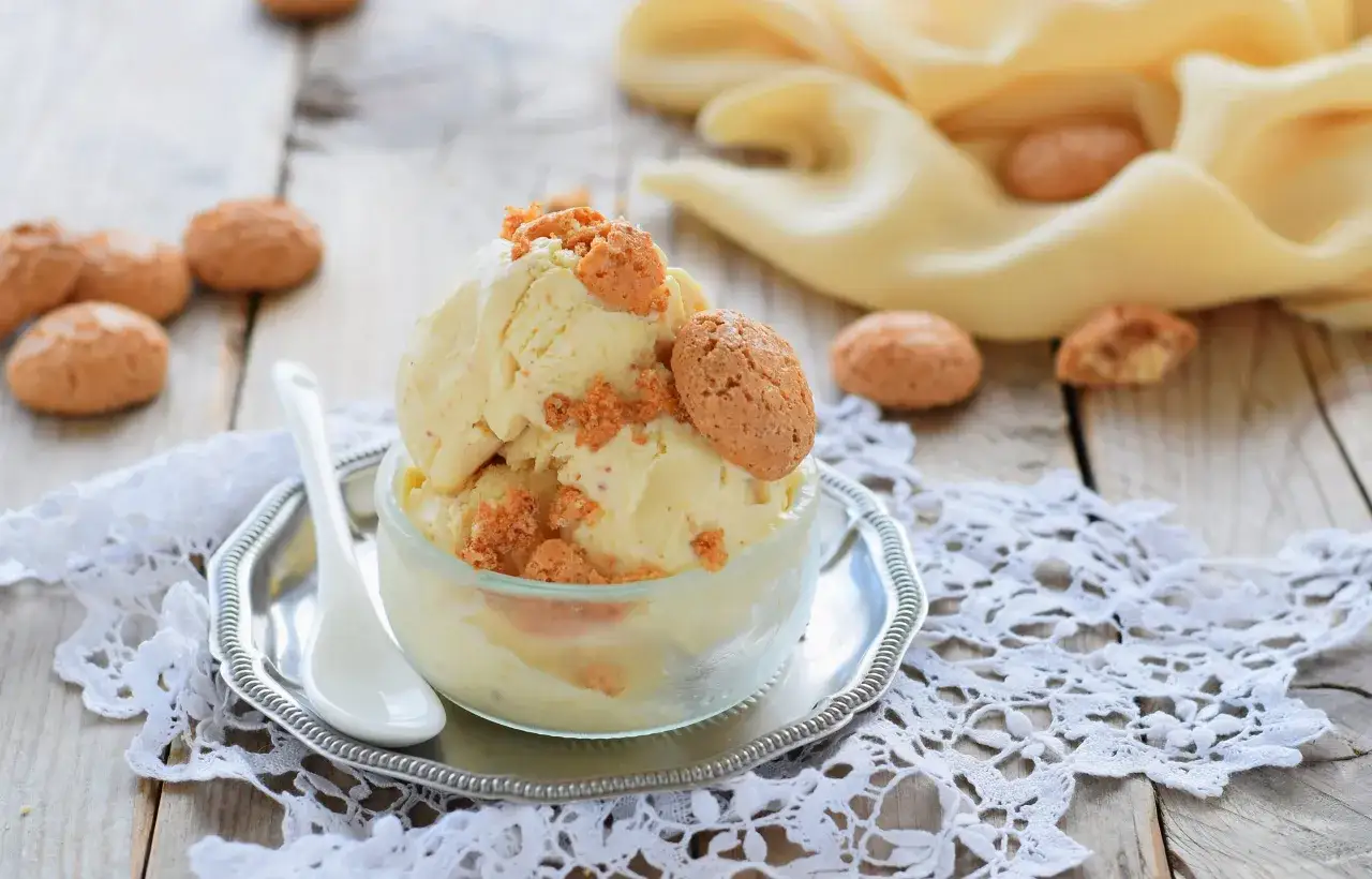 Delizioso gelato amaretto servito in una coppetta di vetro, guarnito con biscotti croccanti e briciole.