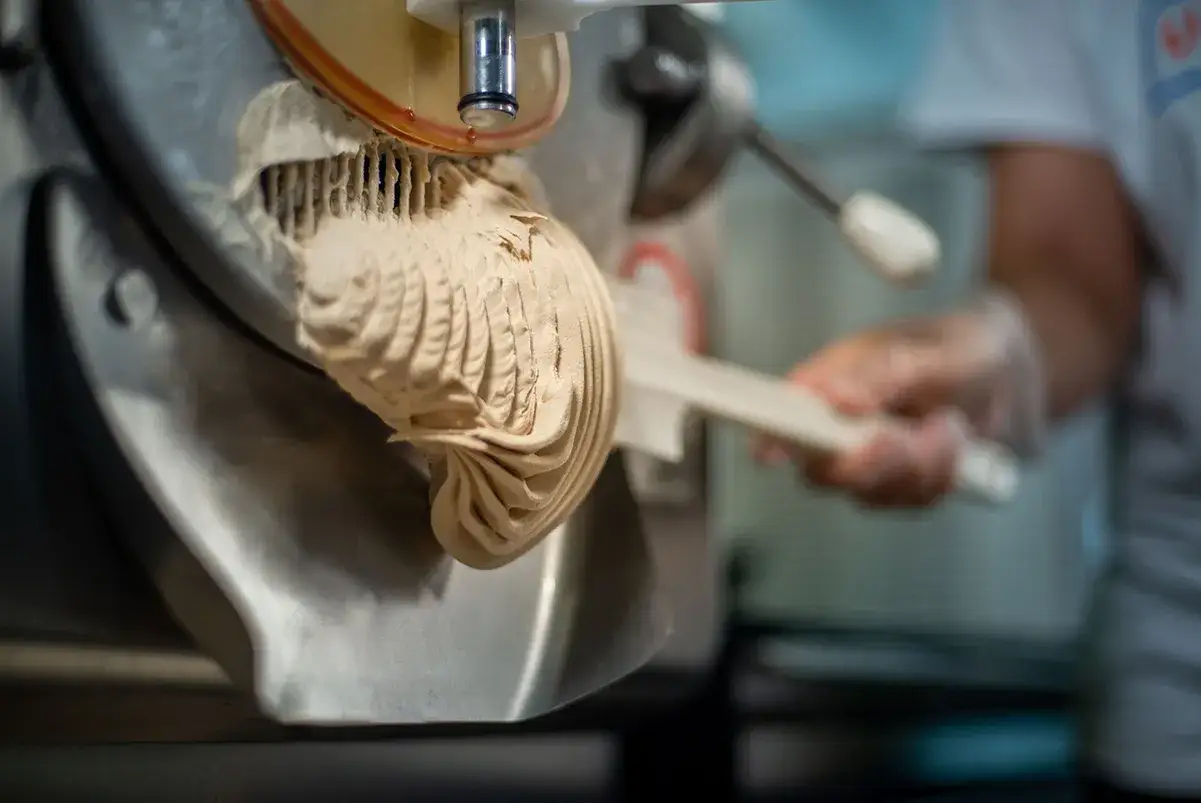 Gelato cremoso esce dalla macchina, mostrando come si fa il gelato professionale. Un artigiano con guanti raccoglie la delizia.