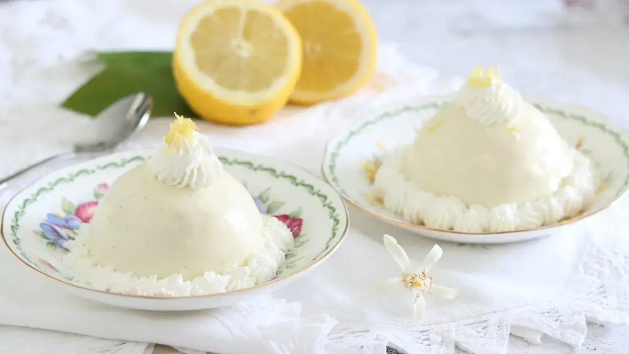 Due delizie al limone, dolci e cremose, decorate con panna e scorza di limone, su piattini floreali.