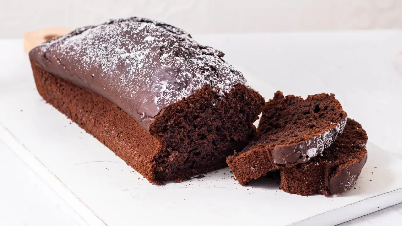 Plumcake al cioccolato soffice e umido, spolverato di zucchero a velo, su un tagliere bianco.