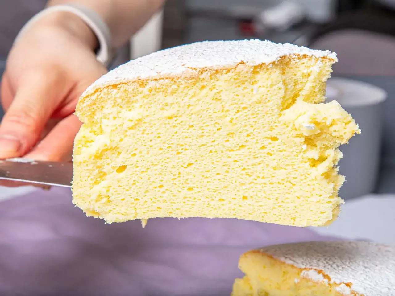 Una fetta soffice e leggera di torta giapponese, cosparsa di zucchero a velo, viene sollevata da una spatola.