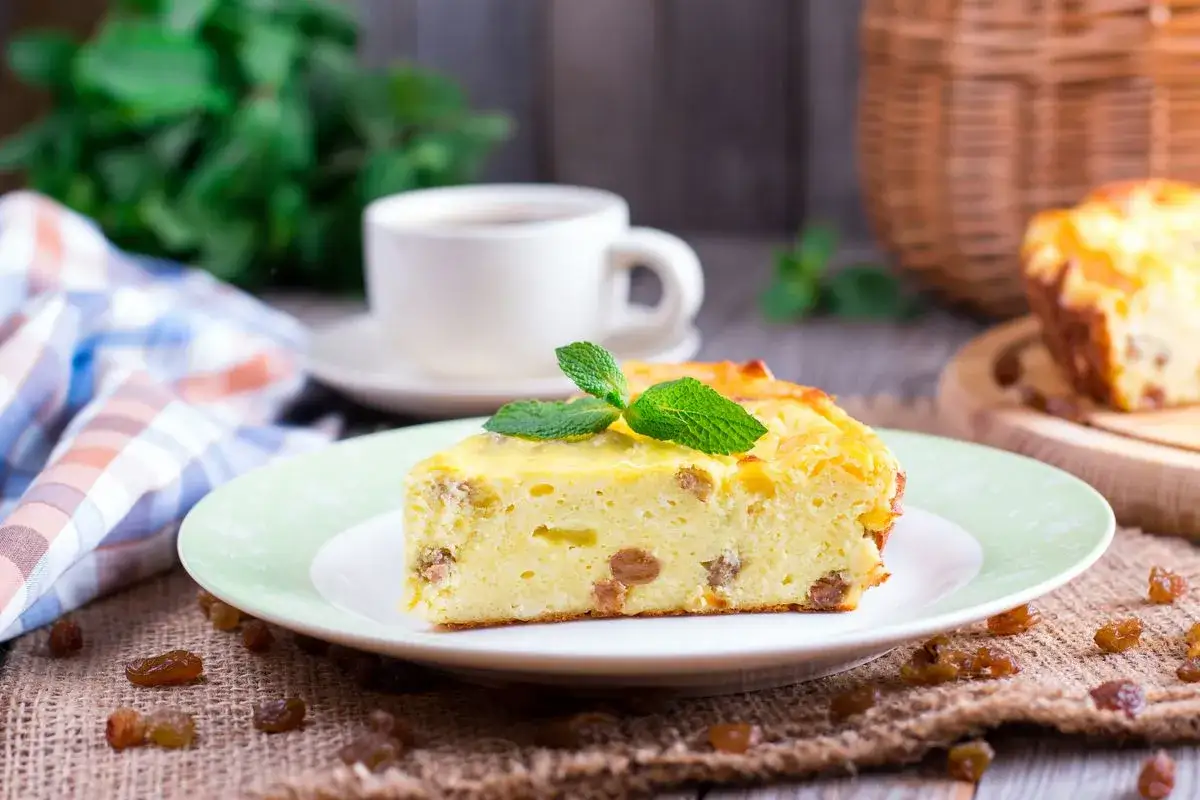 Una fetta di torta putana, soffice e ricca di uvetta, guarnita con menta fresca, accanto a una tazza di caffè.