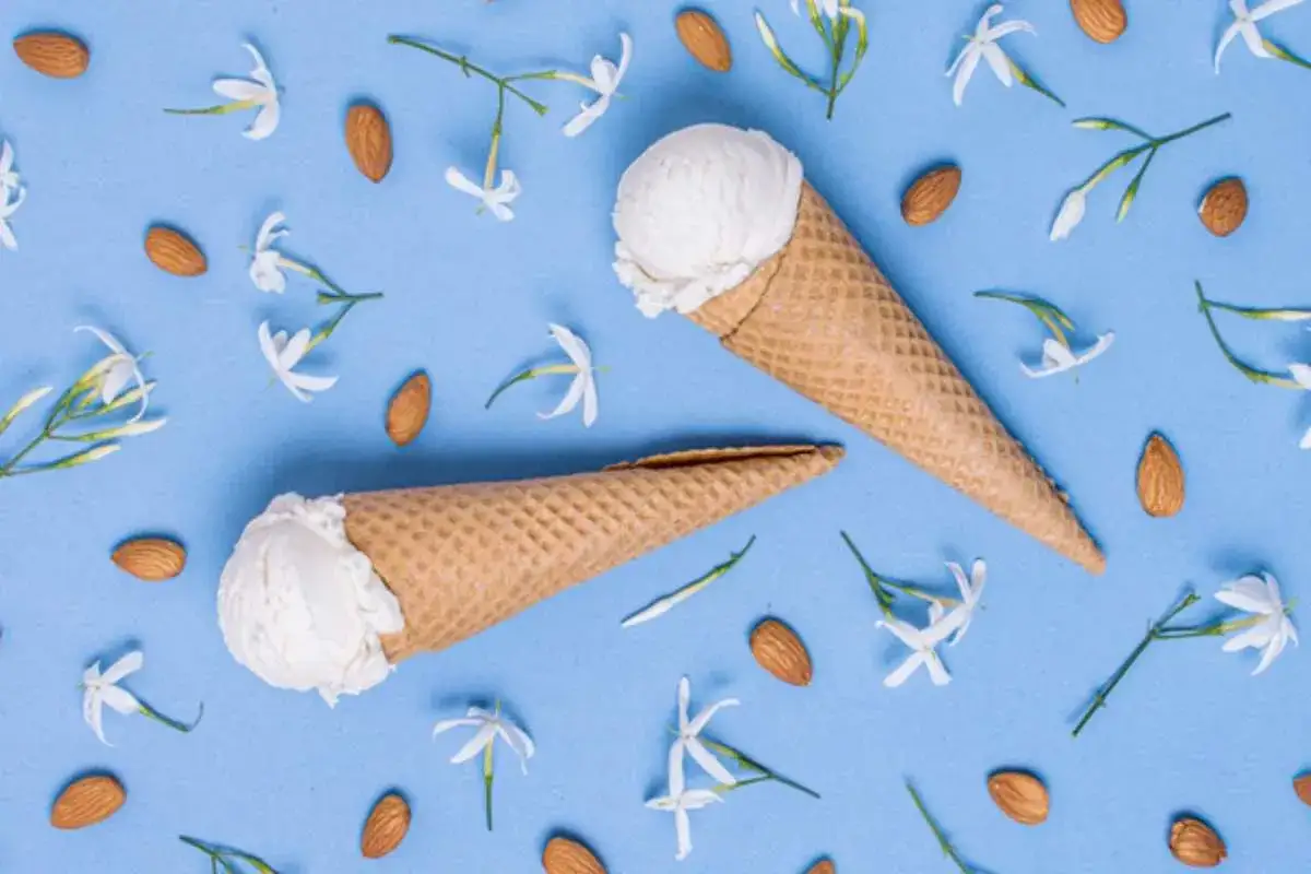 Due coni di gelato al gelsomino, circondati da mandorle e fiori bianchi su sfondo azzurro.