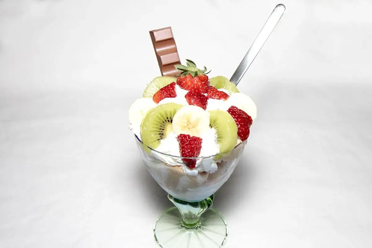 Coppa di gelato con panna montata, fragole, kiwi, banane e una barretta di cioccolato. Un dessert fresco e colorato, perfetto per una pausa golosa.