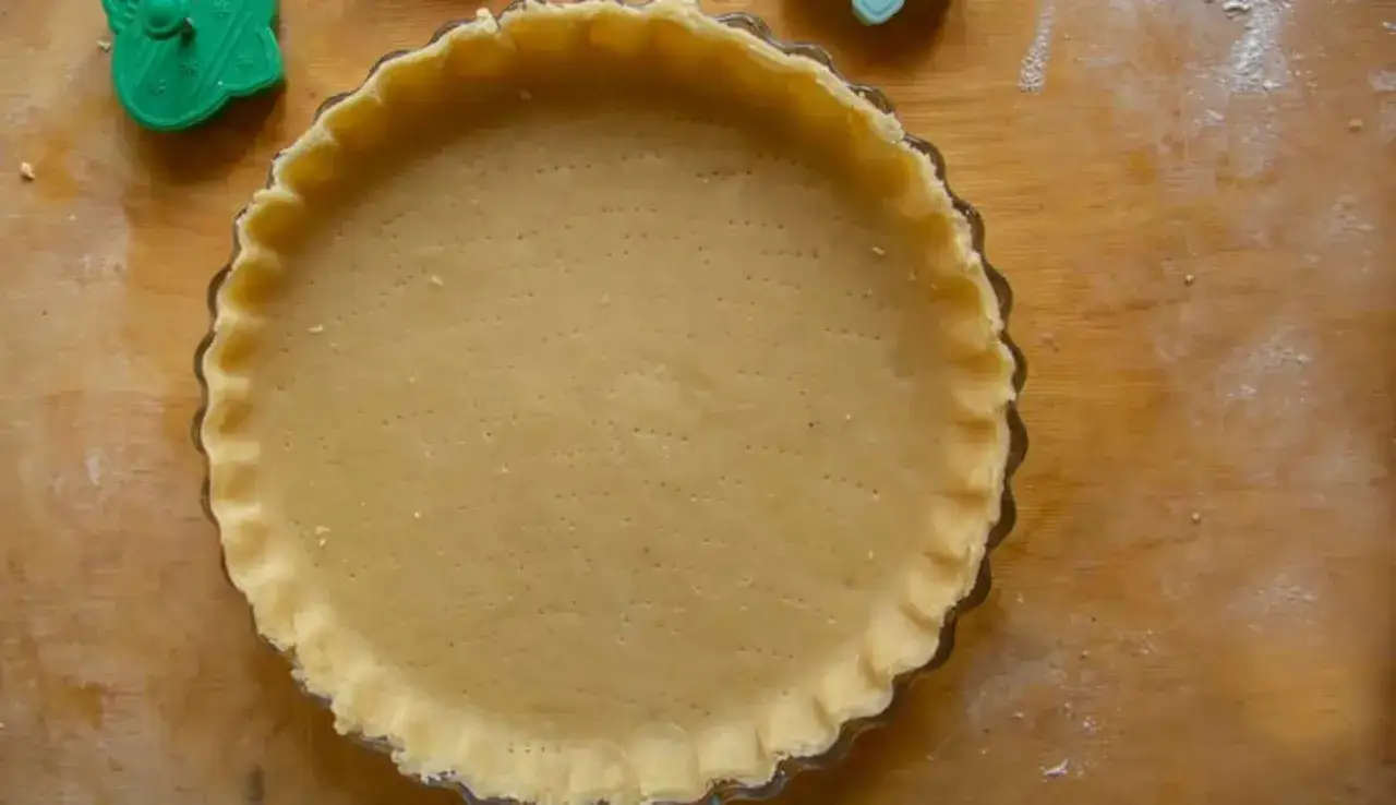 Base di pasta frolla pronta per essere farcita in una tortiera, con stampini verdi sullo sfondo.