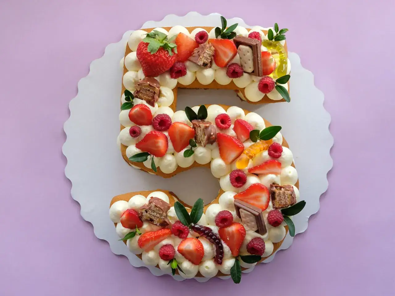 Torta numero 5 decorata con panna, fragole, lamponi, cioccolatini e caramelle gommose.