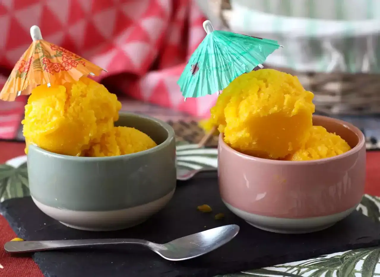 Due coppette con sorbetto al mango, decorate con piccoli ombrellini colorati, pronte per un assaggio estivo.