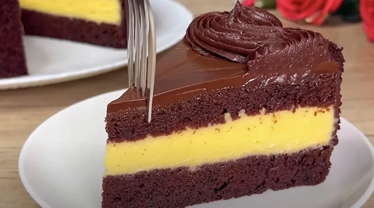Una fetta di pan di spagna al cacao con crema gialla e glassa al cioccolato, pronta per essere gustata.