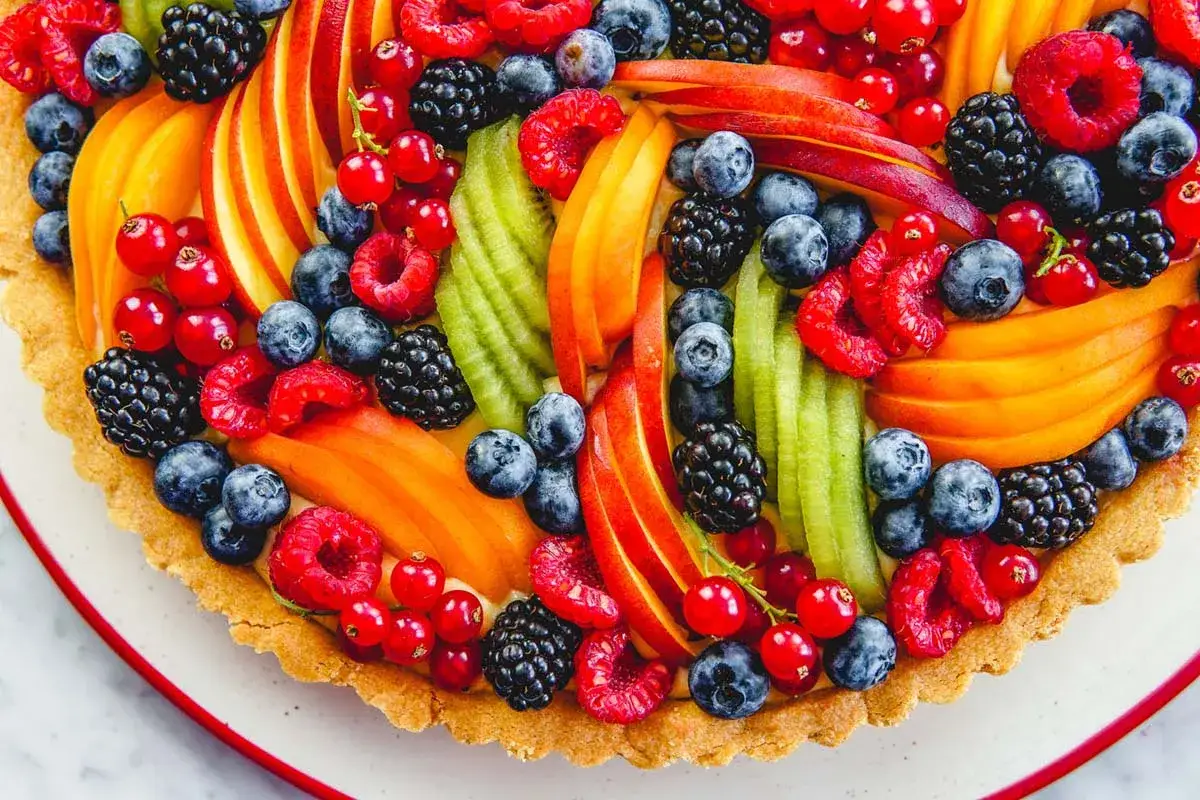 Una colorata torta alla frutta, con pesche, kiwi, lamponi, mirtilli, more e ribes rosso, su una base croccante.