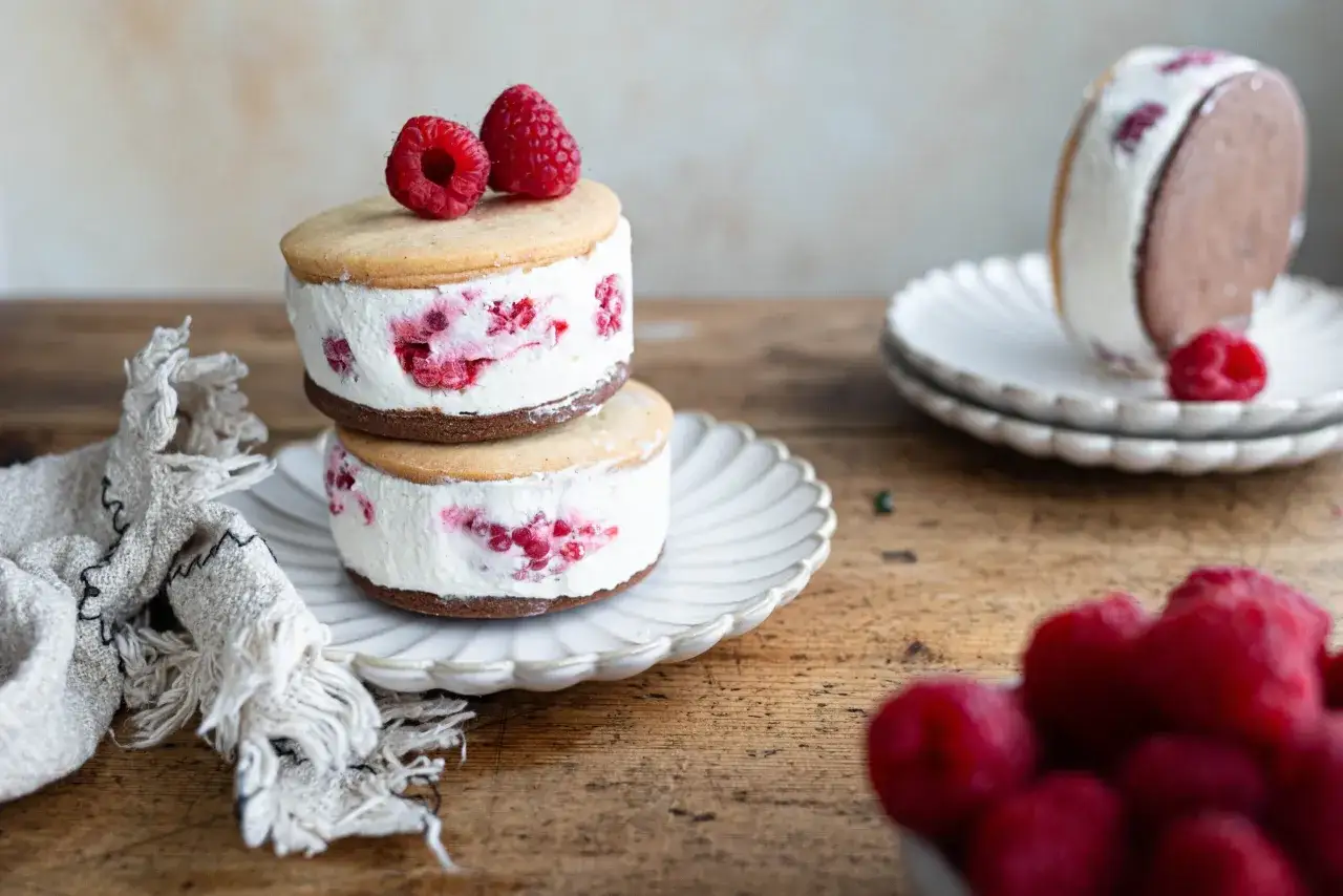 Deliziosa torta gelato con base di biscotti secchi, ripiena di crema e lamponi freschi, guarnita con altri lamponi.
