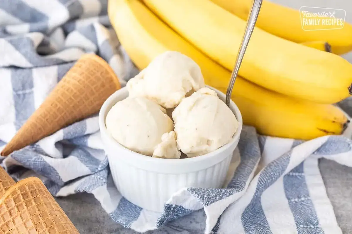 Gelato cremoso servito in una ciotola, con banane mature sullo sfondo. Un'idea per sostituire lo zucchero con la banana per un dolce pi&ugrave; sano.