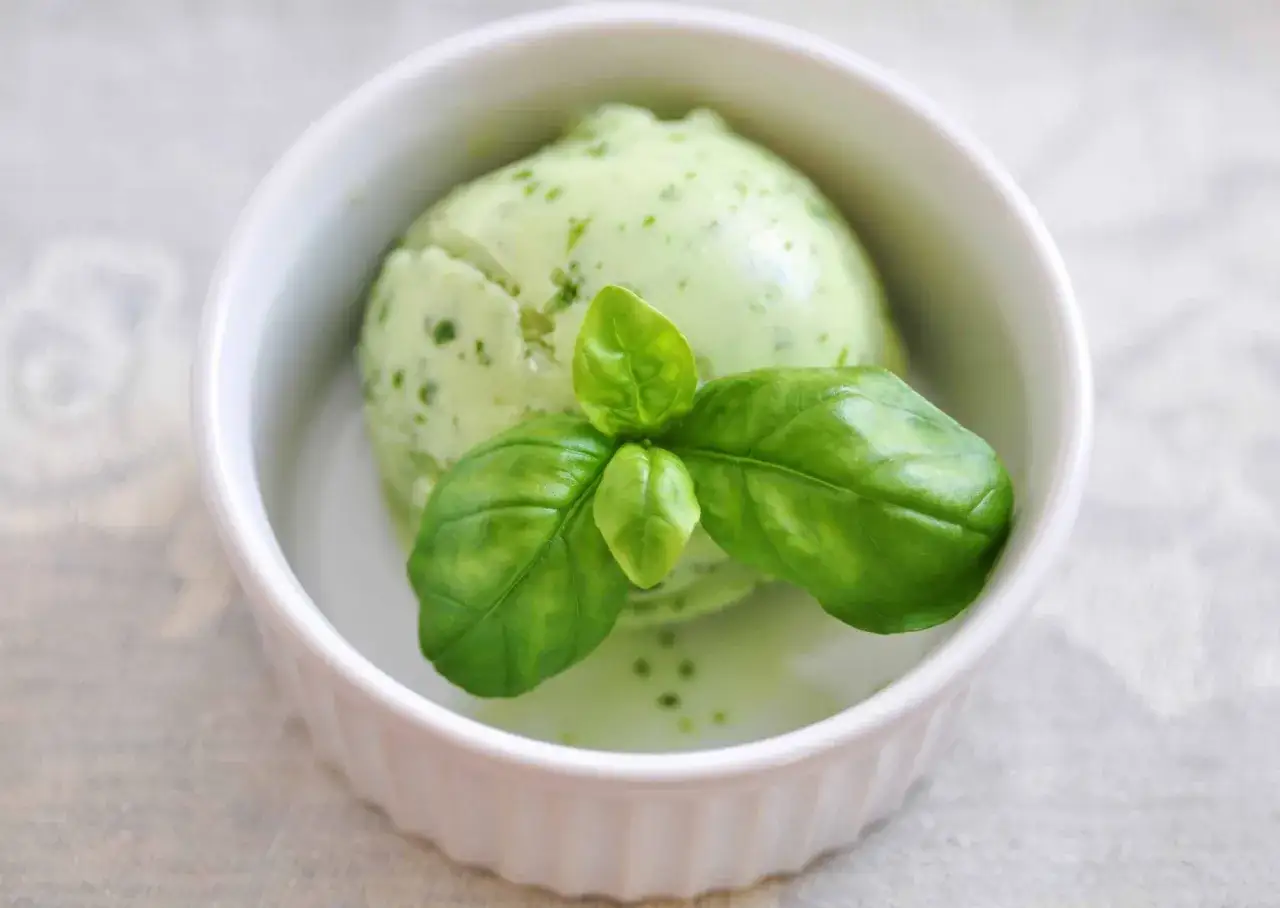 Delizioso gelato al basilico, fresco e profumato, servito in una ciotola bianca con foglie di basilico fresco come guarnizione.