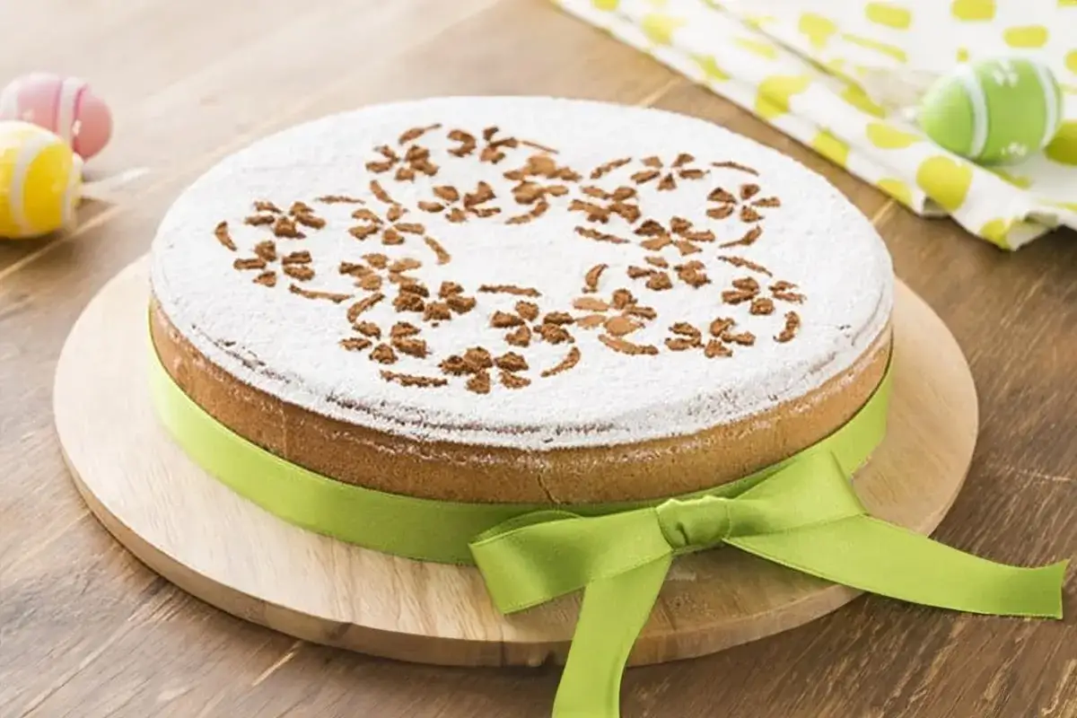 Deliziosa cassata al forno con decorazioni floreali in cacao su zucchero a velo, legata da un nastro verde. Perfetta per la Pasqua.