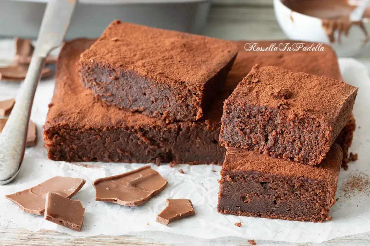 Brownies al cioccolato al latte avanzato, spolverati di cacao, con pezzi di cioccolato e un coltello.