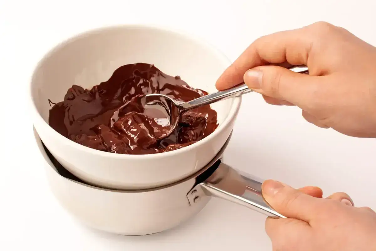 Mani che mescolano cioccolato fuso in una ciotola sopra una pentola, per mantenere liquido il cioccolato sciolto.