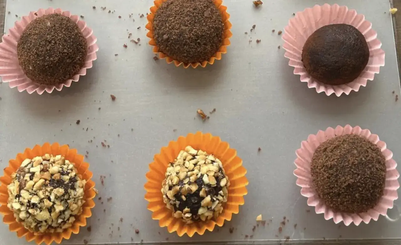 Sei palline di cioccolato fatto in casa con cacao, alcune ricoperte di granella di nocciole, altre di cacao in polvere, in pirottini colorati.