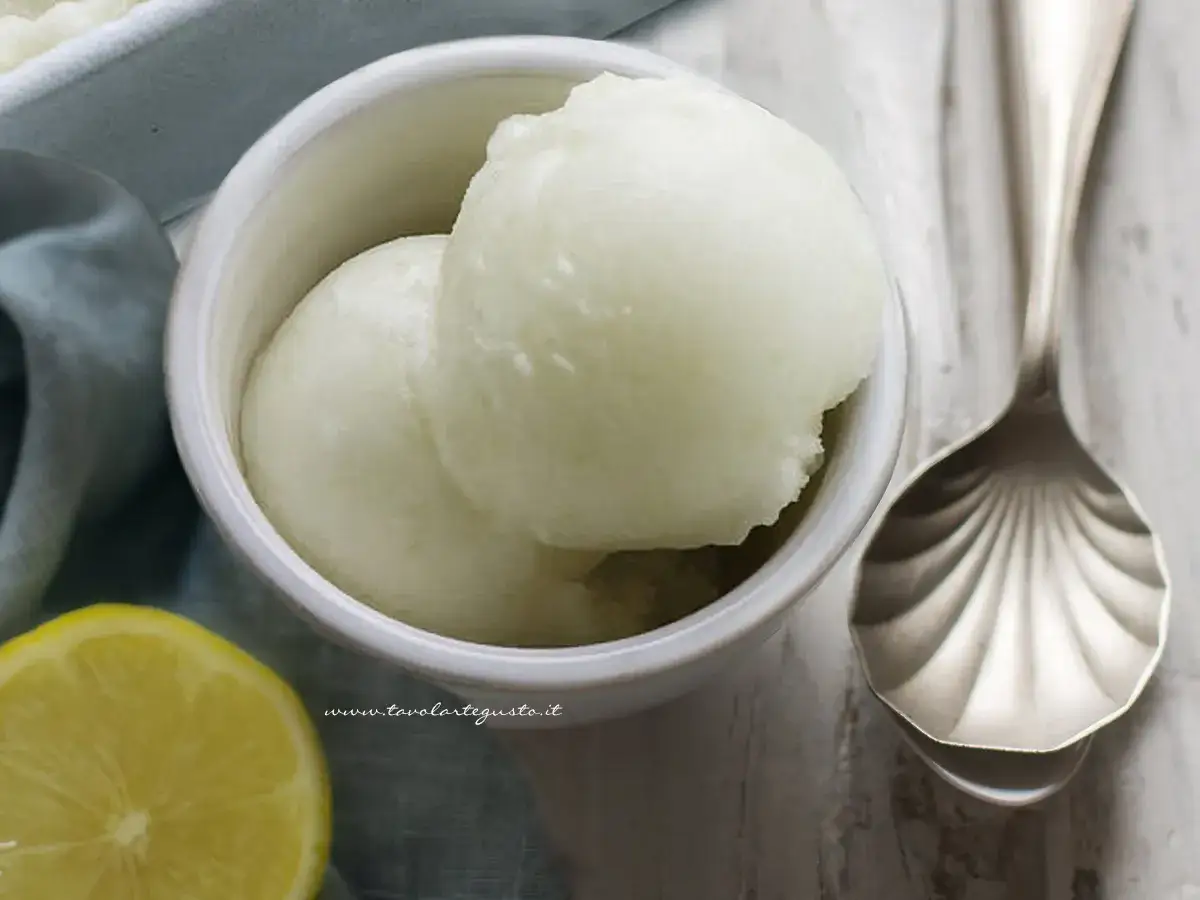 Delizioso sorbetto fatto in casa al limone, servito in una ciotola con una fetta di limone e un cucchiaio decorato.
