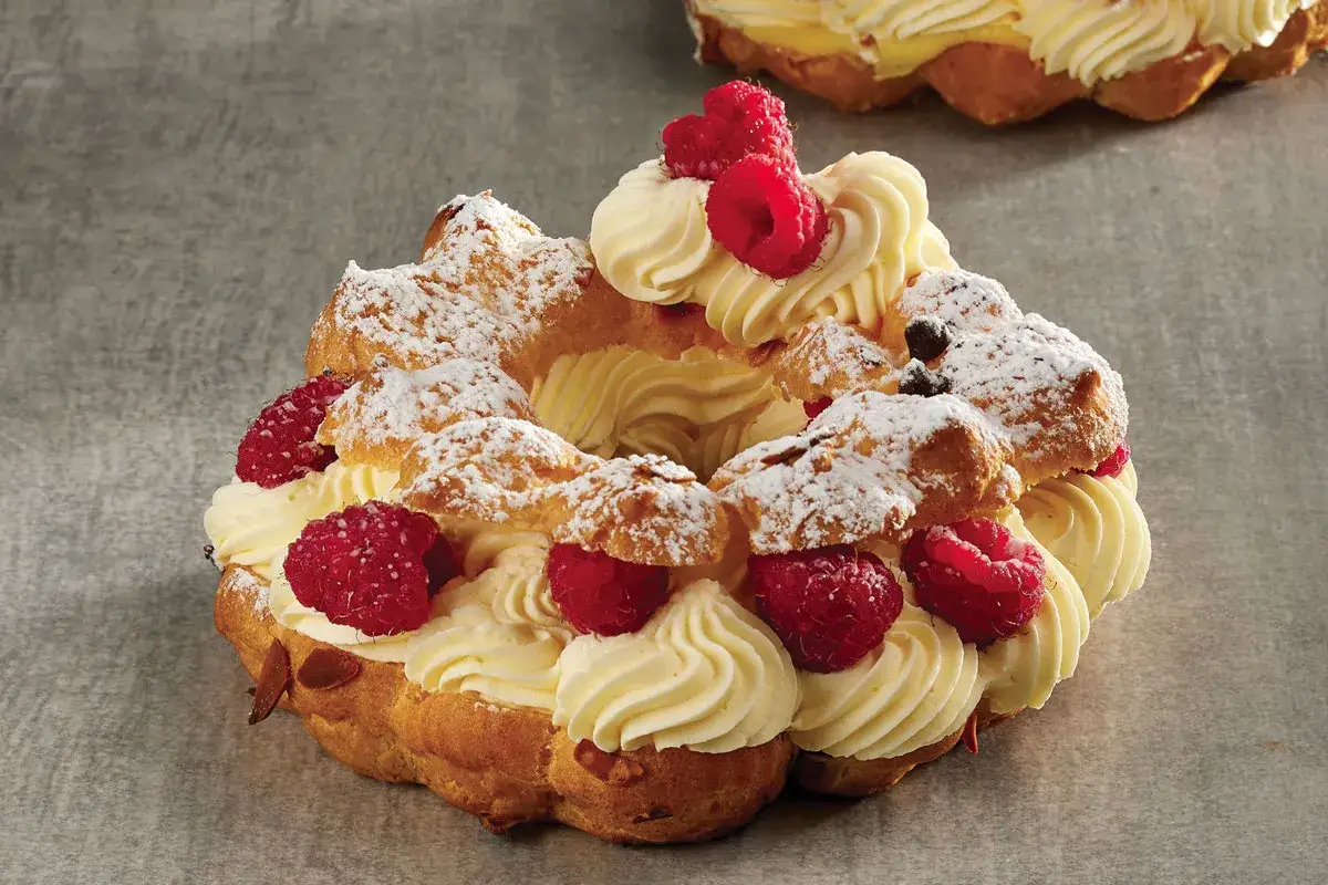 Un delizioso Paris Brest, un anello di pasta choux ripieno di crema diplomatica, decorato con lamponi freschi e zucchero a velo.