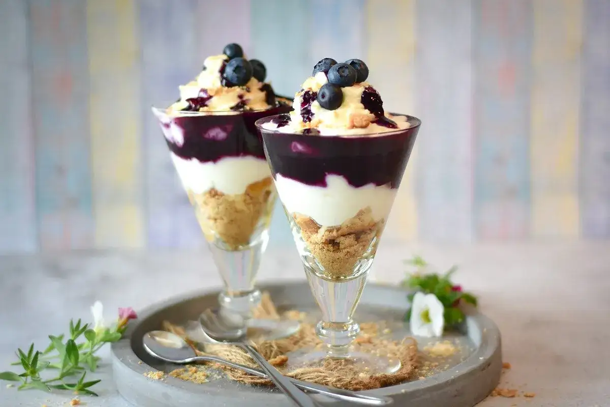 Delizioso gelato con latte, strati di biscotti sbriciolati, crema bianca e mirtilli freschi in coppe eleganti.