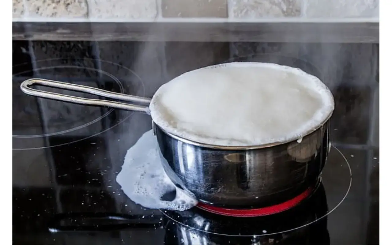 Latte che bolle in una pentola sul fornello, un piccolo trabocco. Impara come pastorizzare il latte in casa in modo sicuro.