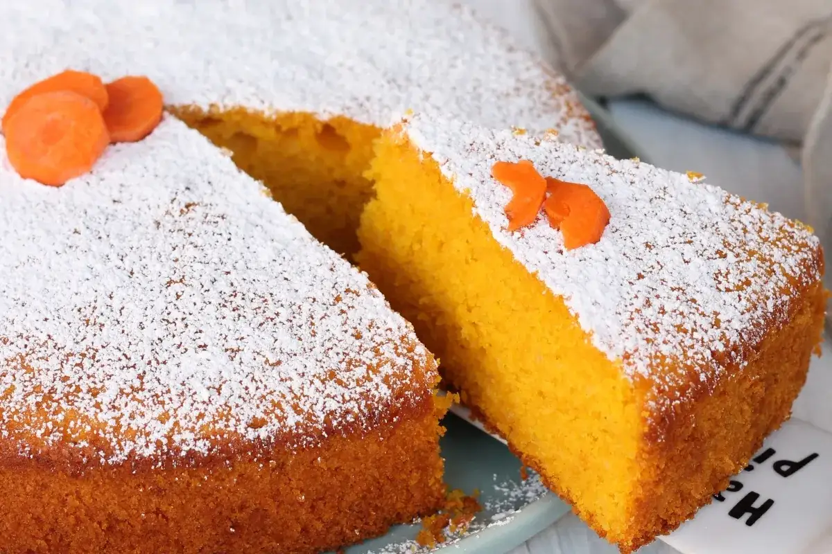 Torta Camilla, ricetta originale: soffice e profumata, con carote e zucchero a velo. Una fetta mostra la sua consistenza perfetta.