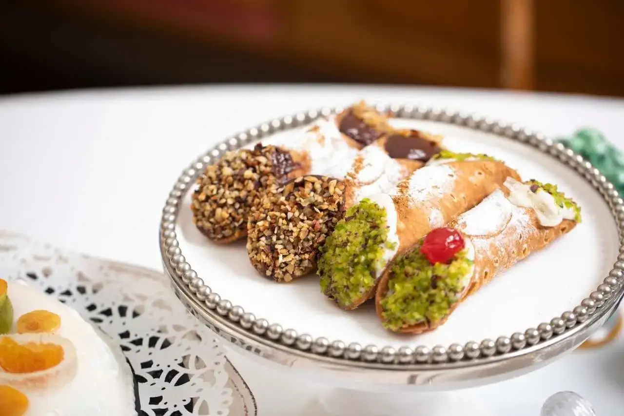 Delizioso cannolo siciliano su un piatto d'argento, guarnito con pistacchi, cioccolato e ciliegina.