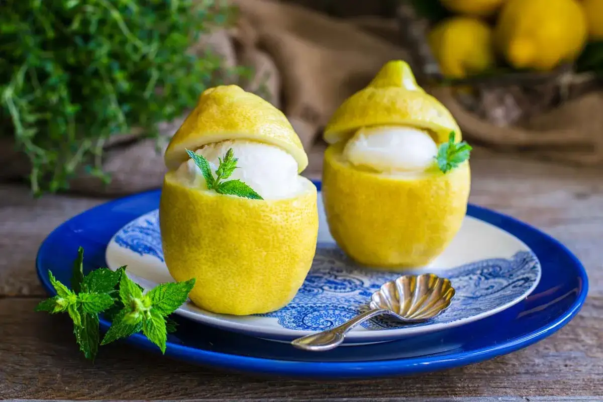 Due limoni scavati, ripieni di gelato al limone veloce e guarniti con menta fresca, su un piatto blu.