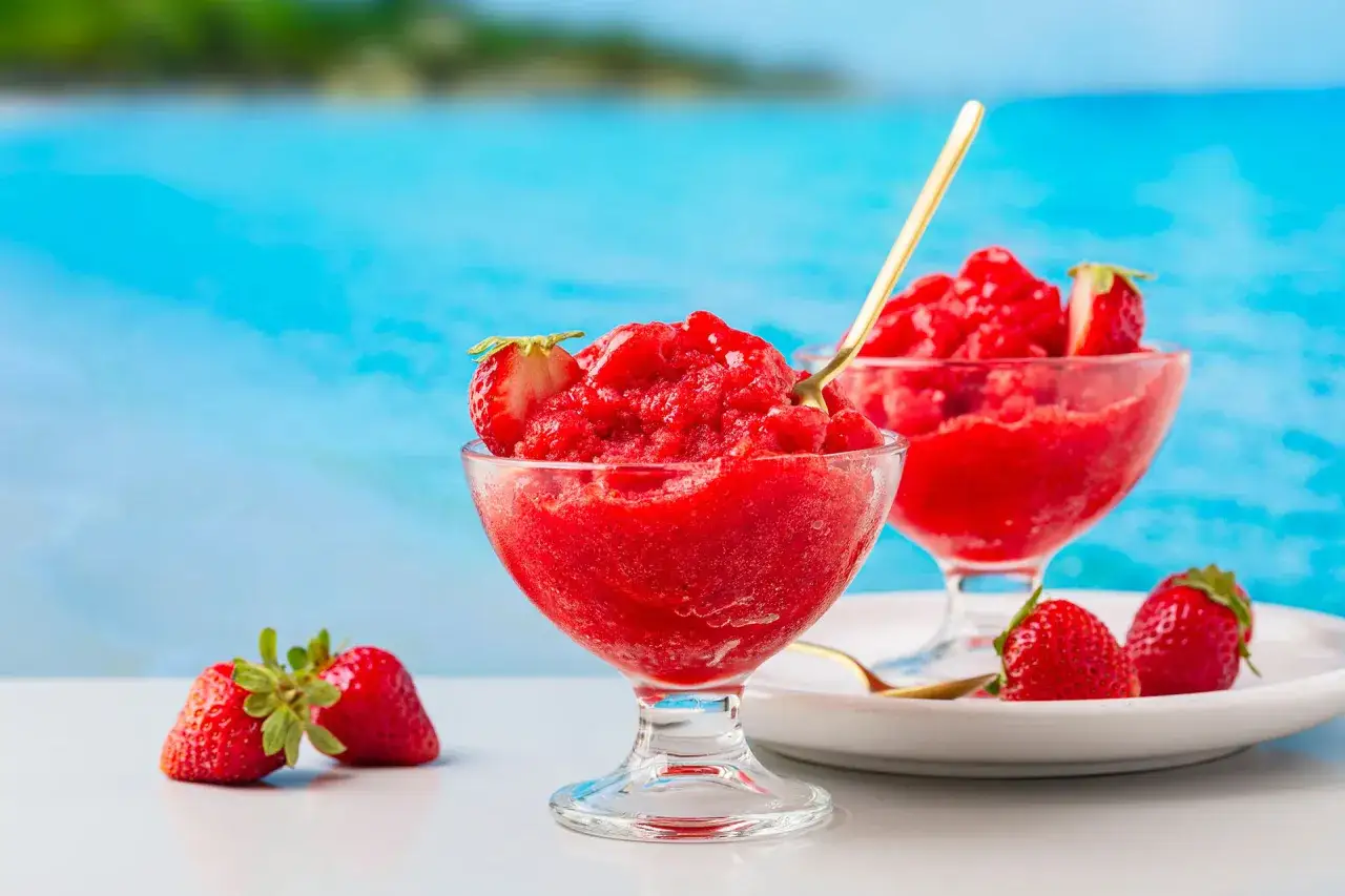 Due coppe di gelato sorbetto alla fragola, con fragole fresche, su sfondo blu mare.