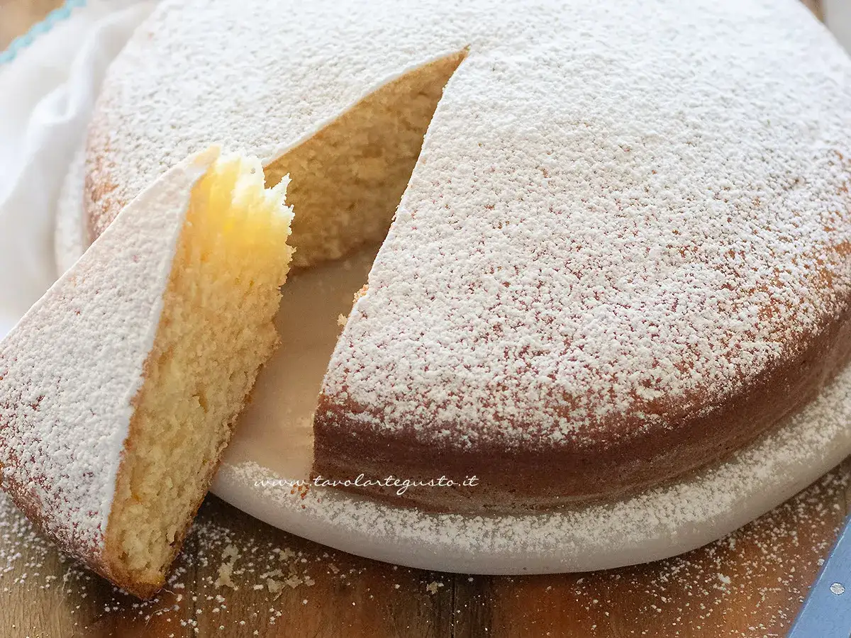 Una soffice torta senza uova, cosparsa di zucchero a velo, con una fetta tagliata che ne rivela la morbidezza.