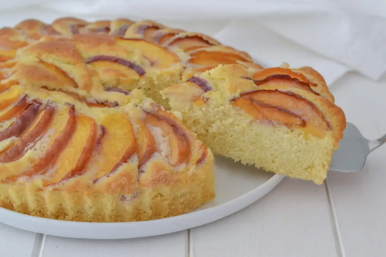 Una fetta di torta di pesche morbidissima, con la sua base soffice e le pesche dorate in superficie, pronta per essere gustata.