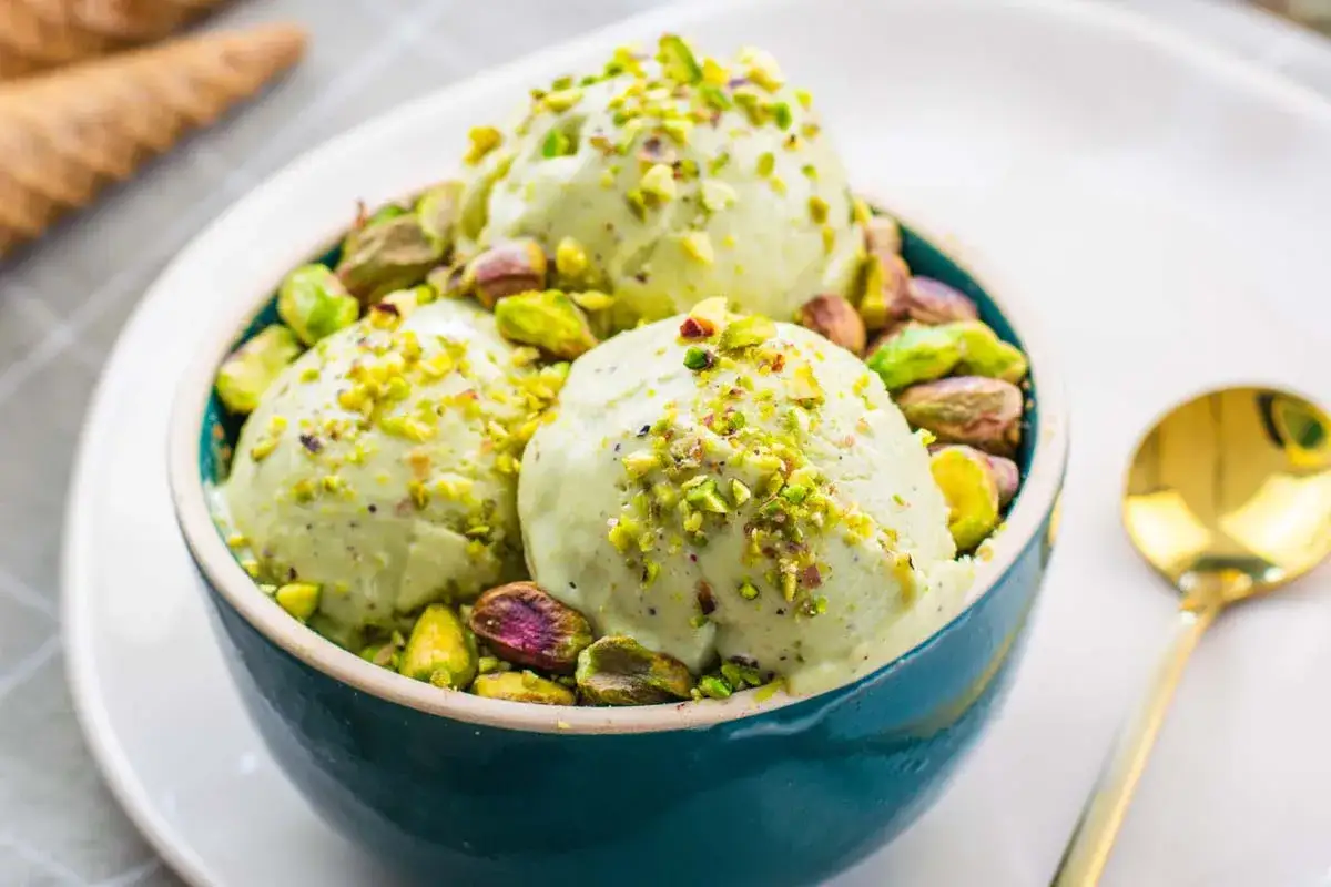 Tre palline di gelato al pistacchio fatto in casa da Benedetta, guarnite con granella e pistacchi interi, in una ciotola blu.