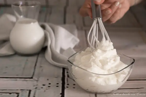 Ecco come fare la panna montata in casa: una ciotola di panna montata soffice, un frullino e una brocca di latte.